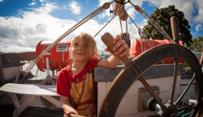 Child seated on a boat holding the steering wheel.