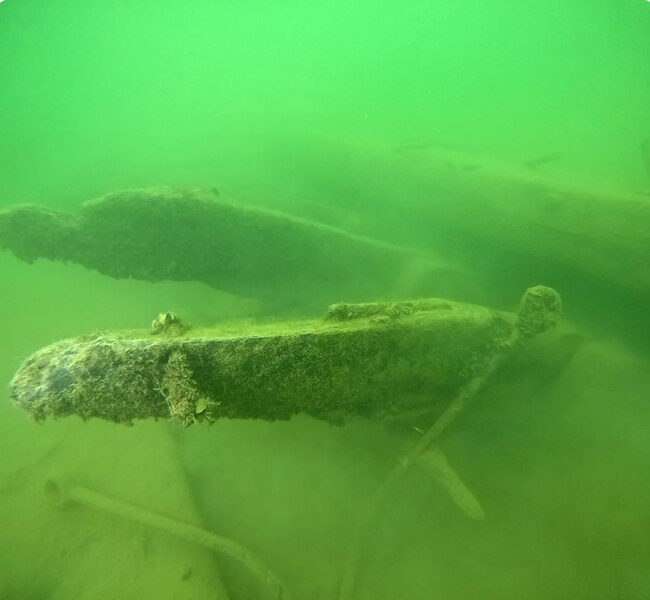 Underwater piece of a shipwreck in murky green water.