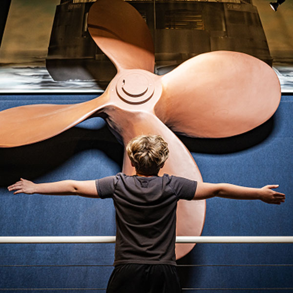 Child standing in front of a large propeller in a museum exhibit.