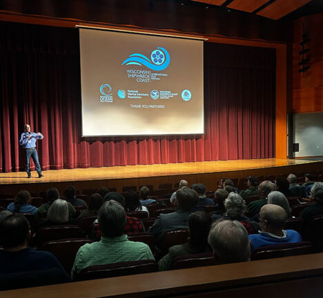 Man presenting on stage in an auditorium.