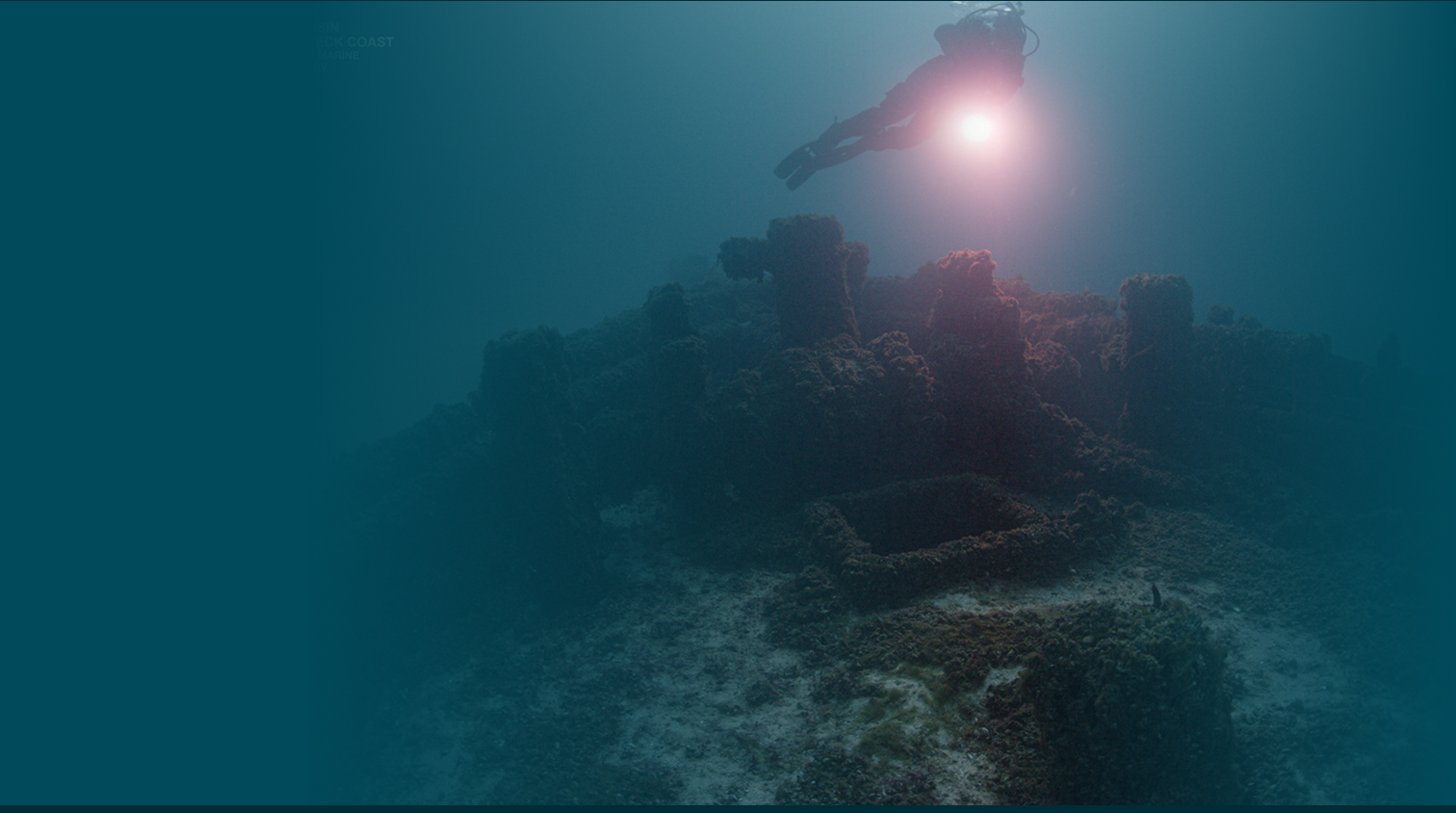 Diver shining a light on a section of a shipwreck underwater.