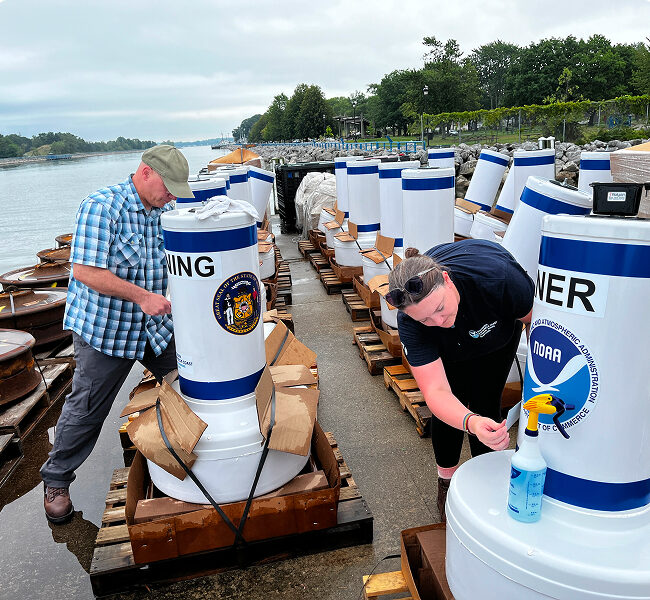 Two people examining a group of buoys on the land near the waters edge.