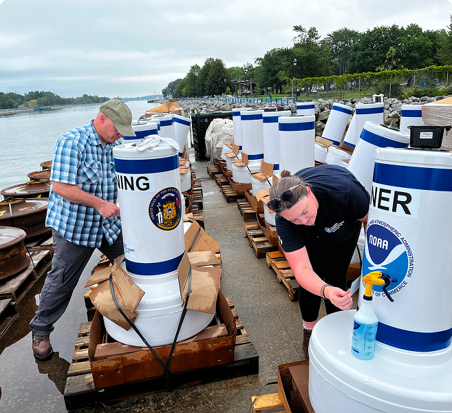 Two people examining a group of buoys on the land near the waters edge.