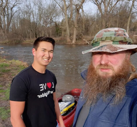 Two people taking a selfie with a kayak along a river.